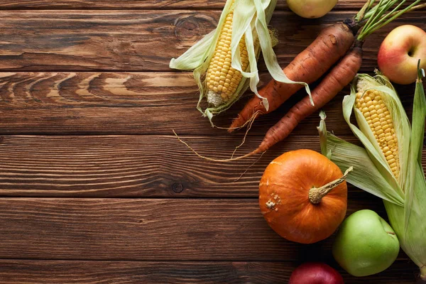 Top view of fresh ripe apples, carrots, pumpkin and sweet corn on brown wooden surface with copy space — Stock Photo