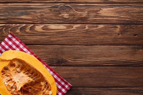 Top view of ripe pumpkin half on checkered tablecloth on brown wooden surface — Stock Photo