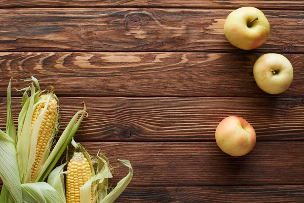 Vista superior de maçãs maduras frescas e milho doce na superfície de madeira marrom com espaço de cópia — Fotografia de Stock