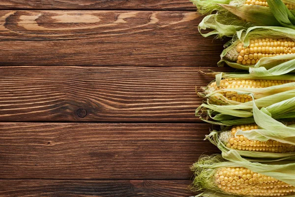 Вид сверху на сырую кукурузу на деревянной поверхности с копировальным пространством — стоковое фото
