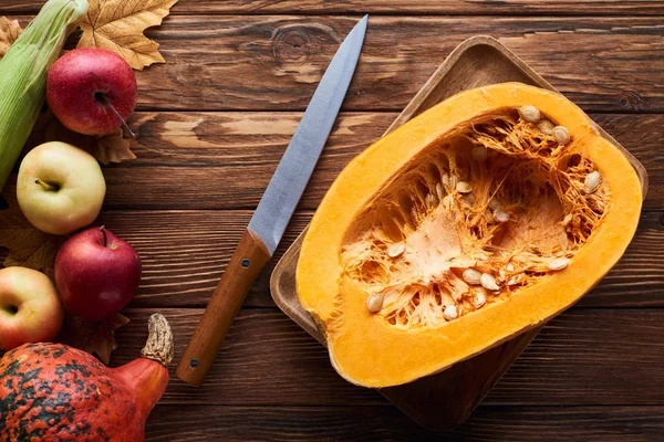 Top view of rectangular dish with fresh pumpkin near knife and apples on brown wooden surface with dry leaves — Stock Photo