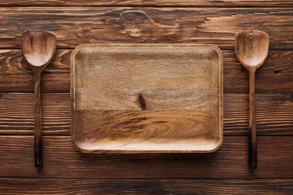 Vue du dessus du plat rectangulaire vide entre les cuillères sur une surface en bois brun avec espace de copie — Photo de stock