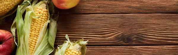 Panoramic shot of fresh apples and sweet corn on brown wooden surface — Stock Photo