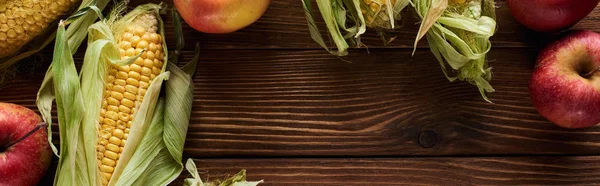 Panoramic shot of fresh apples and sweet corn on brown wooden surface with copy space — Stock Photo