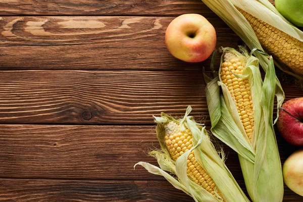 Top view of fresh apples and sweet corn on brown wooden surface — Stock Photo