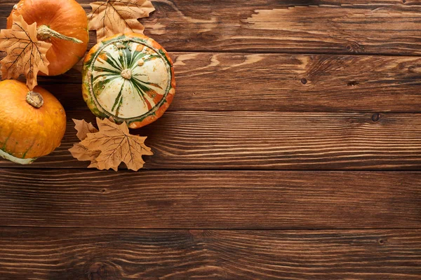 Vue de dessus des citrouilles fraîches sur une surface en bois brun avec des feuilles sèches — Photo de stock