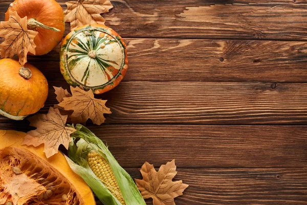 Top view of fresh pumpkins and sweet corn on wooden surface with dry leaves — Stock Photo
