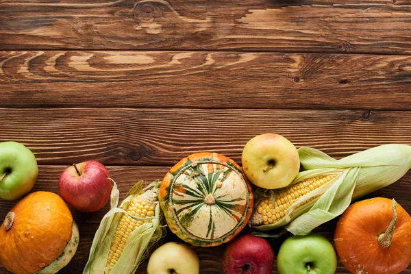 Vista superior de manzanas frescas, calabazas y maíz dulce en la superficie de madera con espacio para copiar - foto de stock
