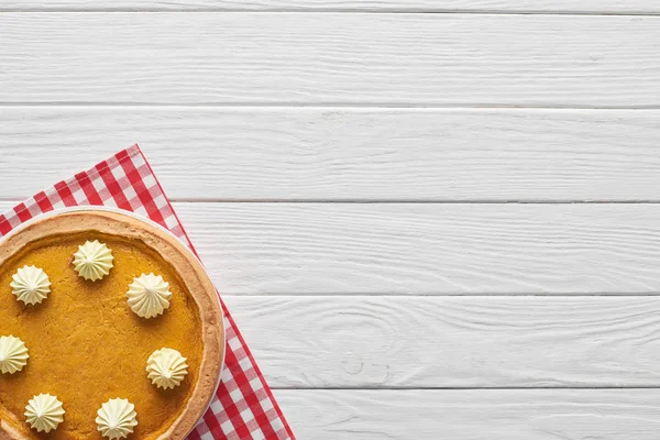 Tasty pumpkin pie with whipped cream on checkered napkin on white wooden surface — Stock Photo