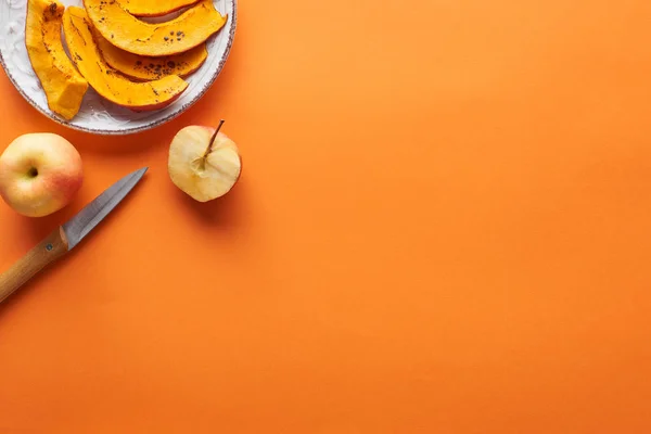Abóbora assada fatiada perto de maçãs inteiras e cortadas e faca na superfície laranja com espaço de cópia — Fotografia de Stock