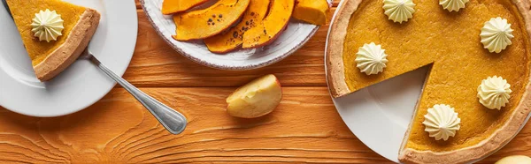 Panoramaaufnahme von köstlichem Kürbiskuchen mit Schlagsahne in der Nähe von gebackenem Kürbis und geschnittenem Apfel auf orangefarbenem Holztisch — Stockfoto