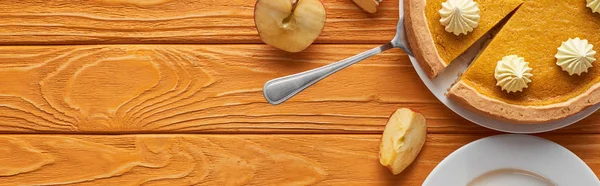 Панорамный снимок вкусного тыквенного пирога со взбитыми сливками возле яблока на оранжевом деревянном столе — стоковое фото