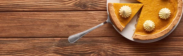 Delicious pumpkin pie with whipped cream on plate with spatula on brown wooden table — Stock Photo
