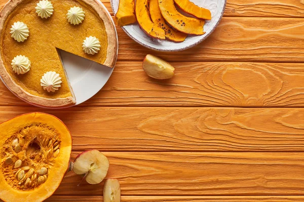 Délicieuse tarte à la citrouille avec crème fouettée près de citrouilles cuites au four et crues, et couper pomme sur table en bois orange — Photo de stock