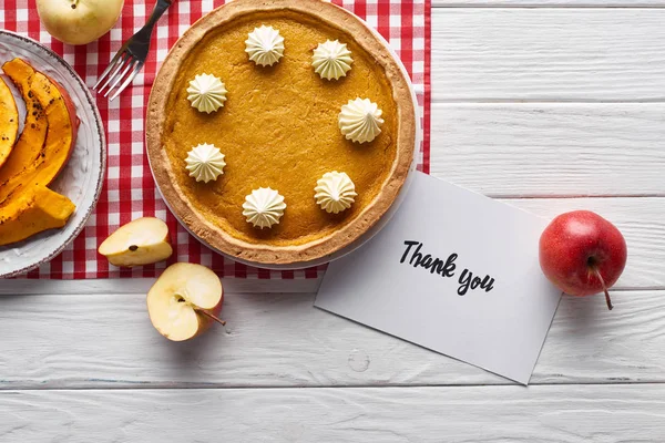 Vista dall'alto di torta di zucca, mele mature e biglietto di ringraziamento su tavolo bianco di legno — Foto stock