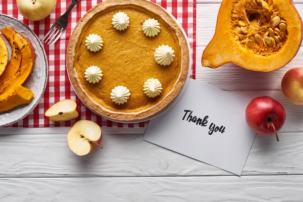 Vista dall'alto di torta di zucca, mele mature e biglietto di ringraziamento su tavolo bianco di legno — Foto stock