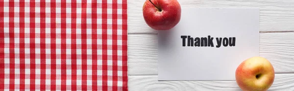 Top view of ripe apples and thank you card on wooden white table with checkered napkin, panoramic shot — Stock Photo