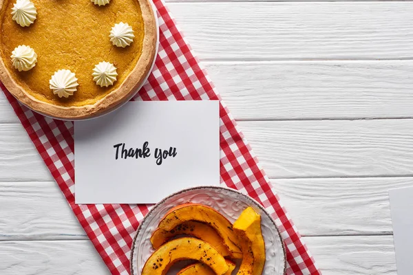 Top view of pumpkin pie, ripe apples and thank you card on wooden white table with red checkered napkin — Stock Photo