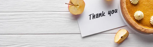 Top view of pumpkin pie, ripe apples and thank you card on wooden white table, panoramic shot — Stock Photo