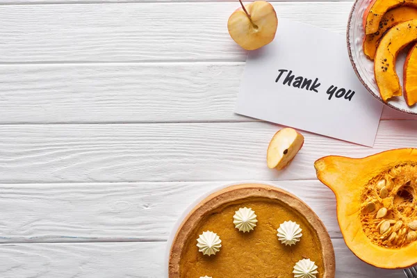 Vue du dessus de tarte à la citrouille, pommes mûres et carte de remerciement sur table blanche en bois — Photo de stock