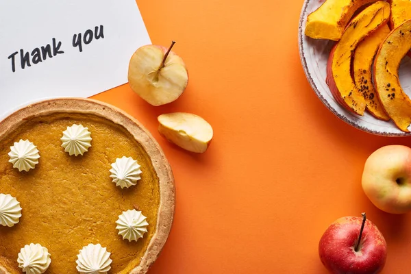 Vista superior de torta de abóbora, maçãs maduras e cartão de agradecimento no fundo laranja — Fotografia de Stock