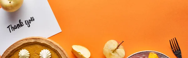 Top view of pumpkin pie, ripe apples and thank you card on orange background with copy space, panoramic shot — Stock Photo