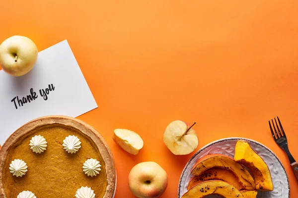 Vista superior de pastel de calabaza, manzanas maduras y gracias tarjeta sobre fondo naranja - foto de stock