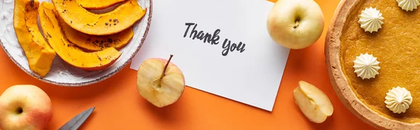 Top view of pumpkin pie, ripe apples and thank you card on orange background, panoramic shot — Stock Photo