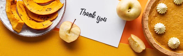Top view of pumpkin pie, ripe apples and thank you card on orange background, panoramic shot — Stock Photo