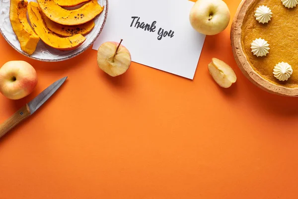 Vista superior da torta de abóbora, maçãs maduras e cartão de agradecimento no fundo laranja com espaço de cópia — Fotografia de Stock