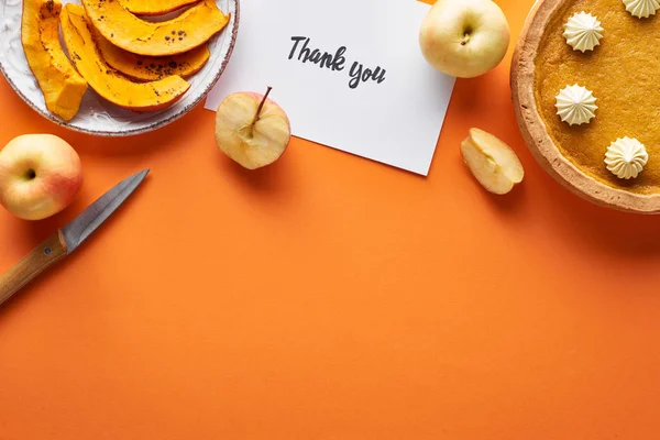 Top view of pumpkin pie, ripe apples and thank you card on orange background with copy space — Stock Photo