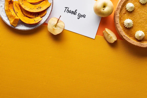 Vista dall'alto di torta di zucca, mele mature e biglietto di ringraziamento su sfondo arancione con spazio di copia — Foto stock