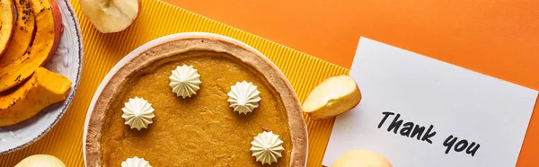 Vue du dessus de tarte à la citrouille, pommes mûres et carte de remerciement sur fond orange, vue panoramique — Photo de stock