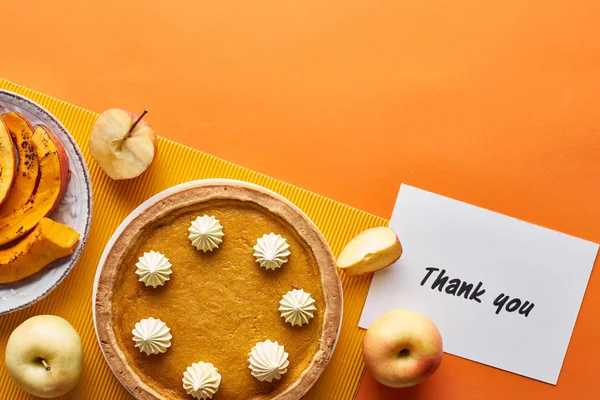 Vue du dessus de tarte à la citrouille, pommes mûres et carte de remerciement sur fond orange — Photo de stock