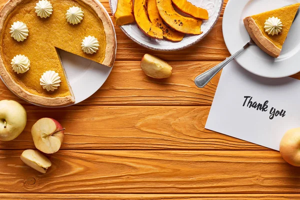 Vue du dessus de tarte à la citrouille, pommes mûres et carte de remerciement sur table en bois — Photo de stock
