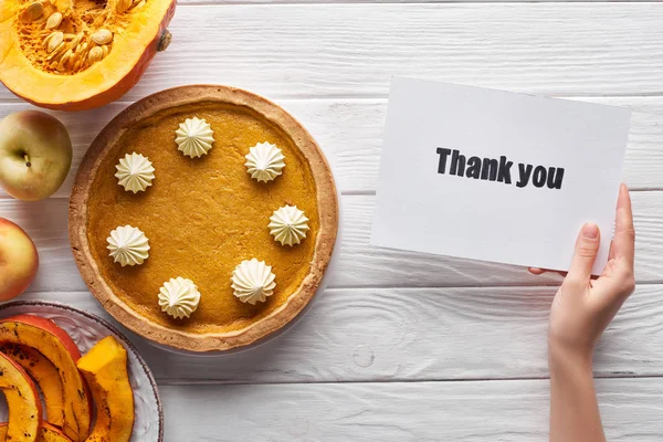 Cropped view of woman holding thank you card near pumpkin pie, ripe apples on white wooden background — Stock Photo