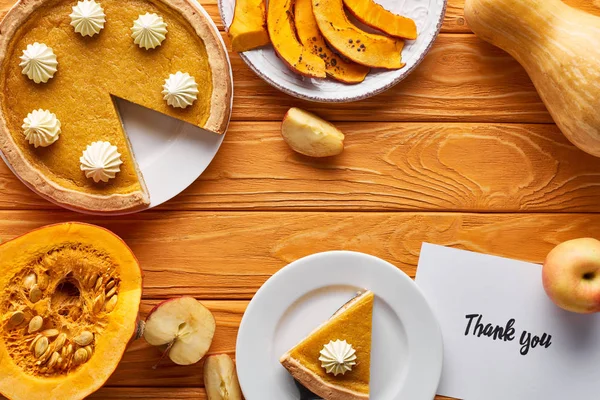 Vue du dessus de tarte à la citrouille, pommes mûres et carte de remerciement sur table en bois — Photo de stock