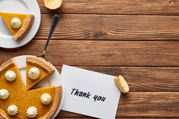 Vue du dessus de tarte à la citrouille, pommes mûres et carte de remerciement sur table brune en bois — Photo de stock