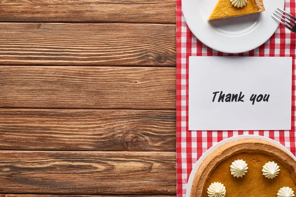 Vista superior del pastel de calabaza y gracias tarjeta en la mesa marrón de madera con servilleta a cuadros rojo - foto de stock