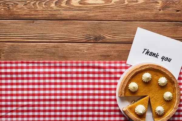 Vue du dessus de tarte à la citrouille et carte de remerciement sur table brune en bois avec serviette à carreaux rouge — Photo de stock