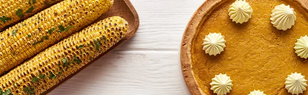 Vista dall'alto della torta di zucca e del mais grigliato servito al tavolo di legno bianco per la cena del Ringraziamento — Foto stock