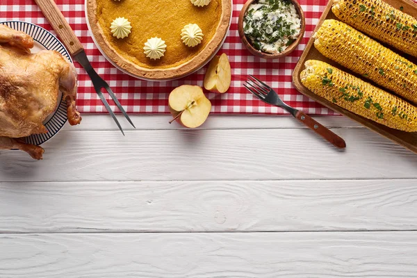 Blick von oben auf Kürbiskuchen, Truthahn und Gemüse, serviert am weißen Holztisch zum Erntedank-Abendessen mit rot kariertem Tuch — Stockfoto