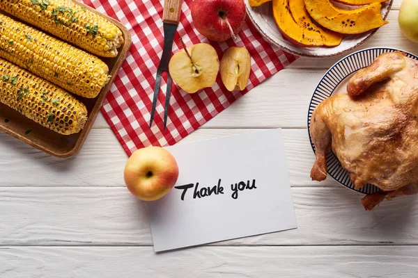 Vista superior de pastel de calabaza, pavo y verduras servidas en la mesa de madera blanca con tarjeta de agradecimiento para la cena de Acción de Gracias - foto de stock