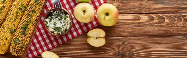 Blick von oben auf gegrilltes Mais und Äpfel, serviert auf rotkarierter Serviette am Holztisch zum Erntedank-Abendessen, Panoramaaufnahme — Stockfoto