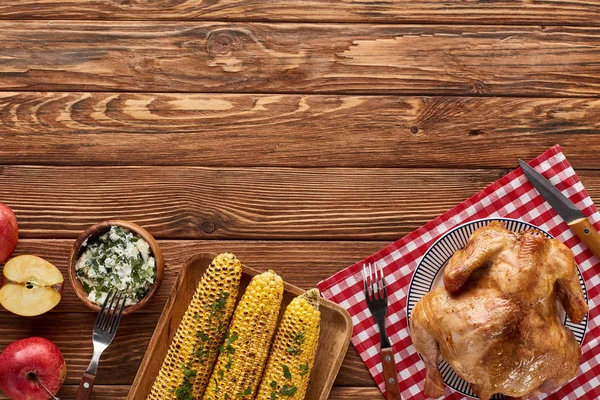 Top view of roasted turkey and grilled corn served on red checkered napkin at wooden table for Thanksgiving dinner — Stock Photo