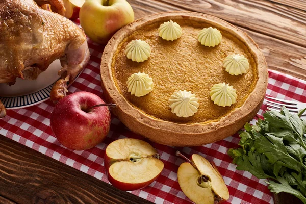 Pumpkin pie, roasted turkey and apples on red checkered napkin at wooden table for Thanksgiving dinner — Stock Photo