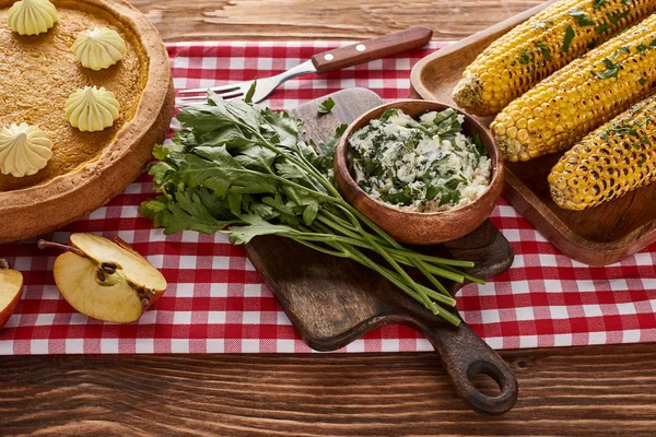 Pumpkin pie, grilled corn and parsley on red checkered napkin at wooden table for Thanksgiving dinner — Stock Photo