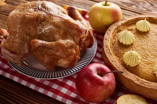 Pumpkin pie, roasted turkey and apples on red checkered napkin at wooden table for Thanksgiving dinner — Stock Photo