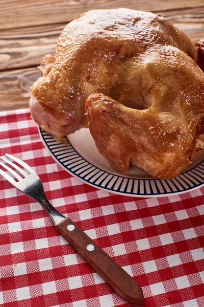 Roasted turkey and fork served on red checkered napkin at wooden table for Thanksgiving dinner — Stock Photo
