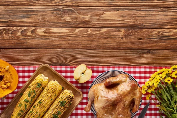 Vista superior de pavo asado y verduras servidas en la mesa de madera cerca de flores amarillas para la cena de Acción de Gracias - foto de stock